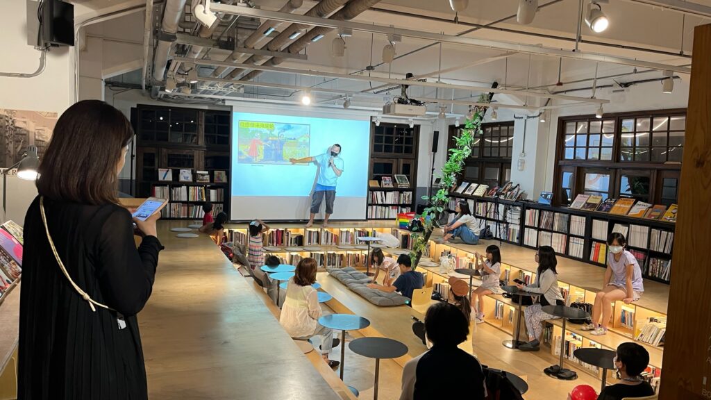 段床のイベントスペースで読み聞かせを楽しむ子どもたちと周囲の本棚