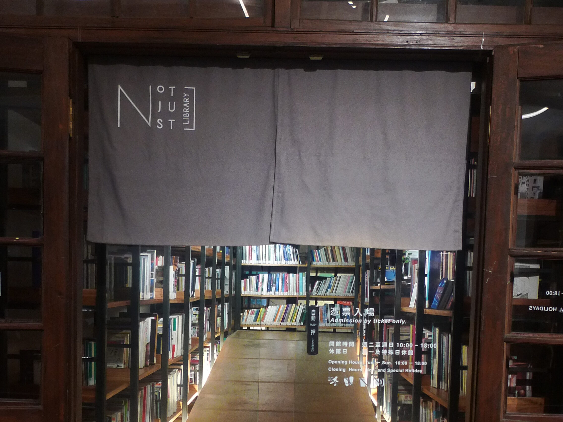 Not Just Libraryの暖簾付きエントランス。棚越しに本が並ぶ、チケット制の案内表示
